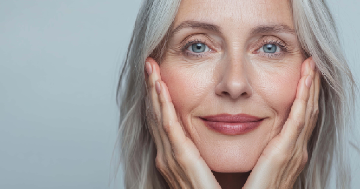 Mature woman with gray hair holding her face, showing healthy skin after Sculptra treatment in Yukon, OK